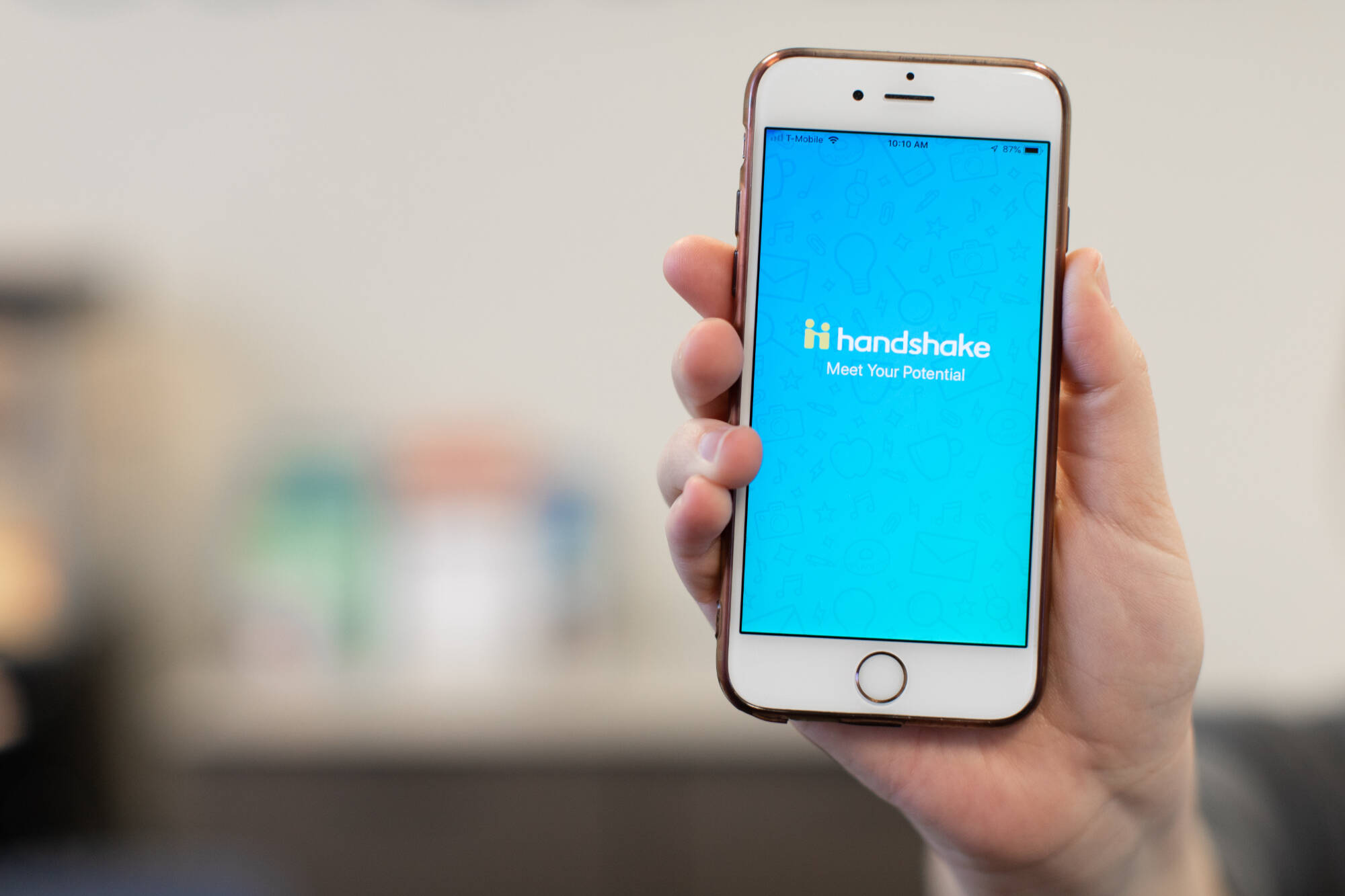 A hand holds a smartphone displaying the "Handshake" app, featuring a blue background with the text "handshake" and the subtitle "Meet Your Potential."